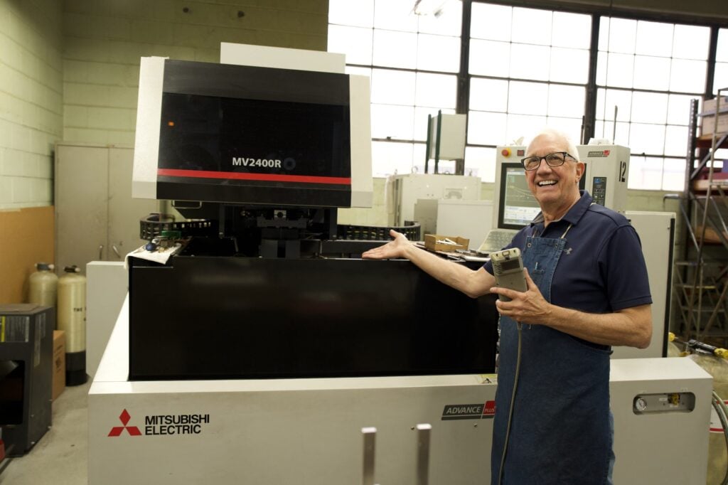 Manor Tool & Manufacturing team member beside a Mitsubishi wire EDM machine, photographed by TMC Marketing